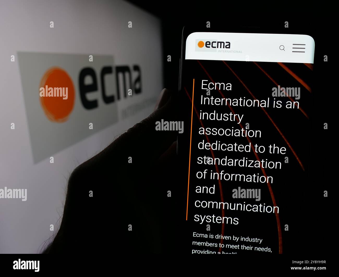 Persona che detiene lo smartphone con il sito web dell'organizzazione di standard Ecma International sullo schermo davanti al logo. Messa a fuoco al centro del display del telefono. Foto Stock