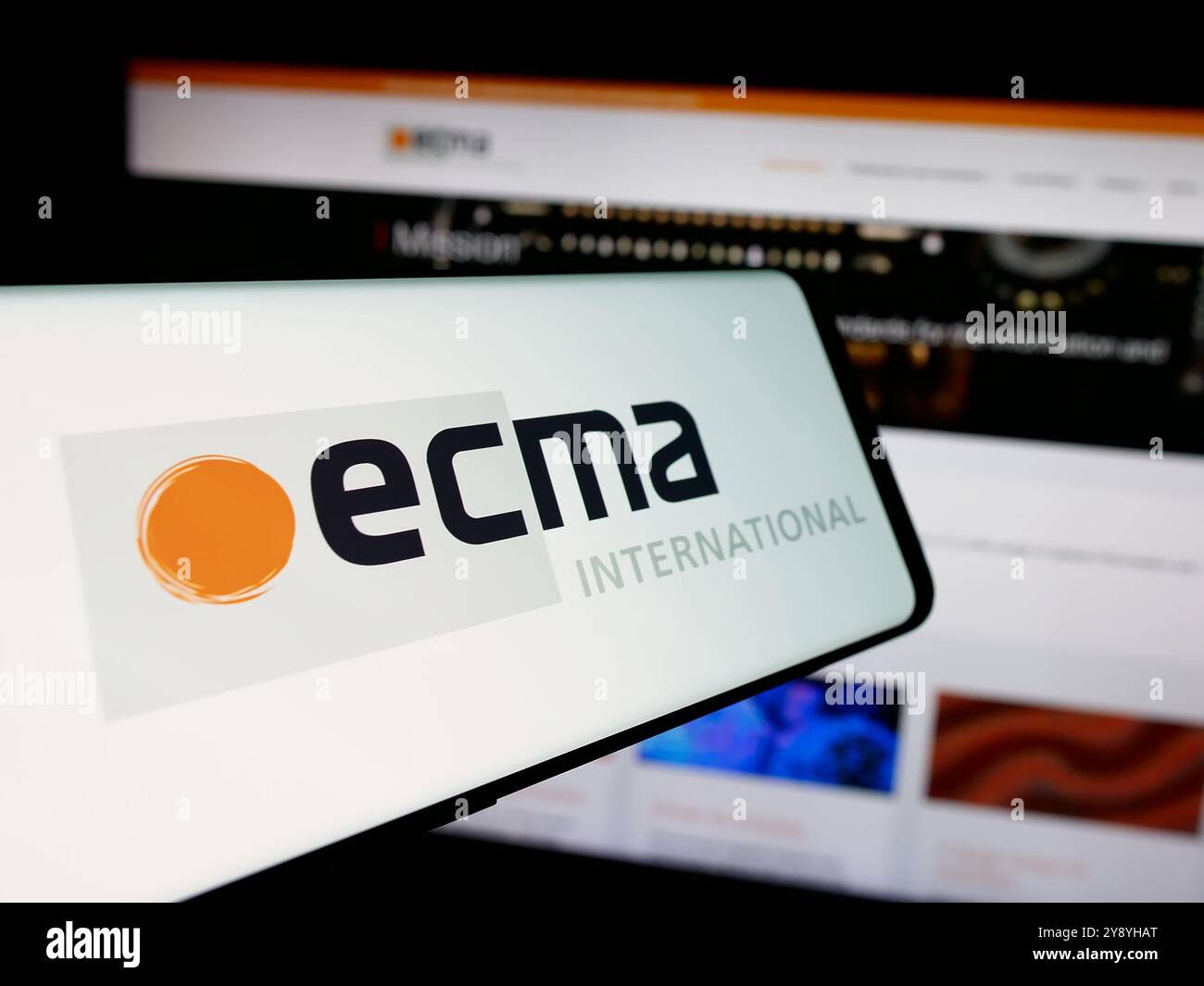 Telefono cellulare con logo dell'organizzazione di standard Ecma International sullo schermo di fronte al sito Web. Messa a fuoco al centro del display del telefono. Foto Stock