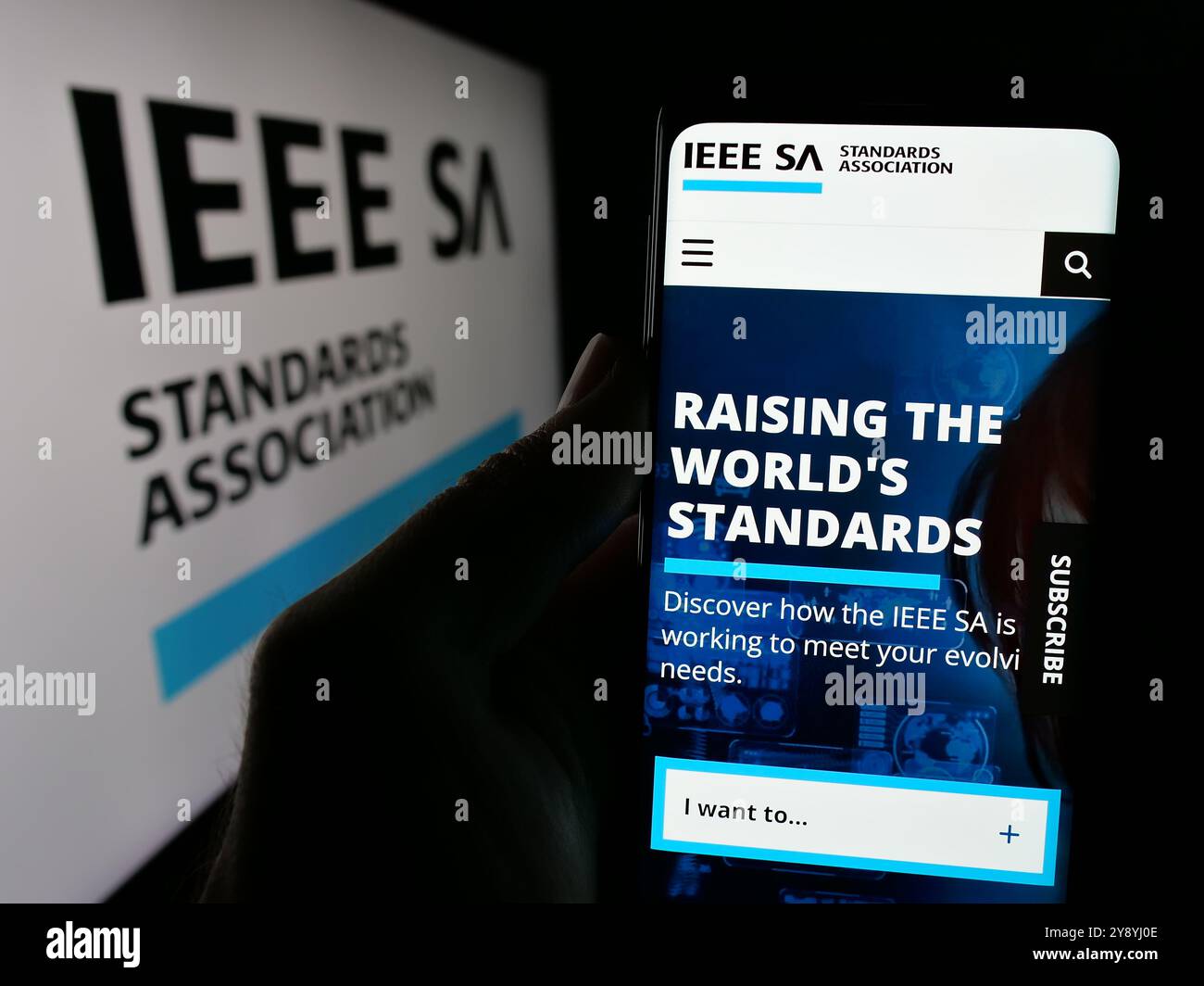 Persona che detiene un cellulare con il sito Web della IEEE Standards Association sullo schermo davanti al logo. Messa a fuoco al centro del display del telefono. Foto Stock
