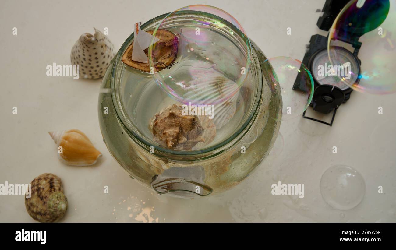 Una barca di noci in un vaso di vetro pieno d'acqua. Una bussola, conchiglie, bolle di sapone. Foto Stock