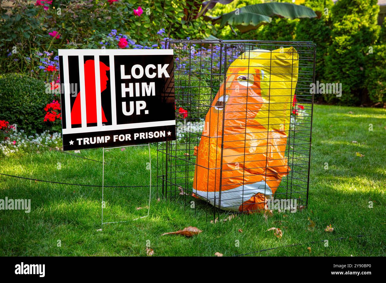 Un'esposizione del 2024 per le elezioni presidenziali con un segno anti-Donald Trump e una figura arancione brillante del personaggio gonfiabile di Trump in una gabbia. Foto Stock