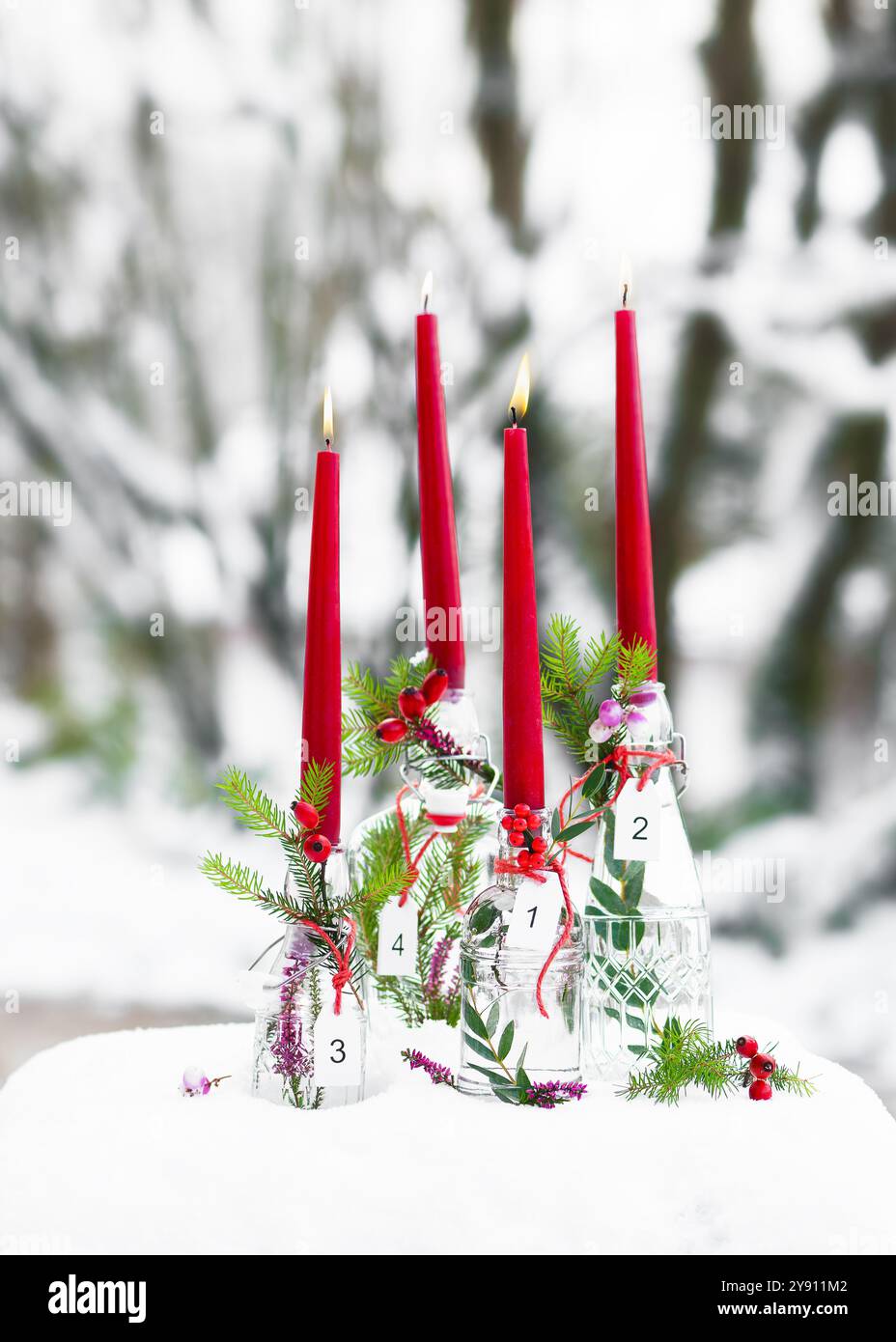 Corona dell'Avvento con quattro candele rosse e pendenti bianchi in legno in bottiglie di vetro decorate con rami di abete. Foto Stock
