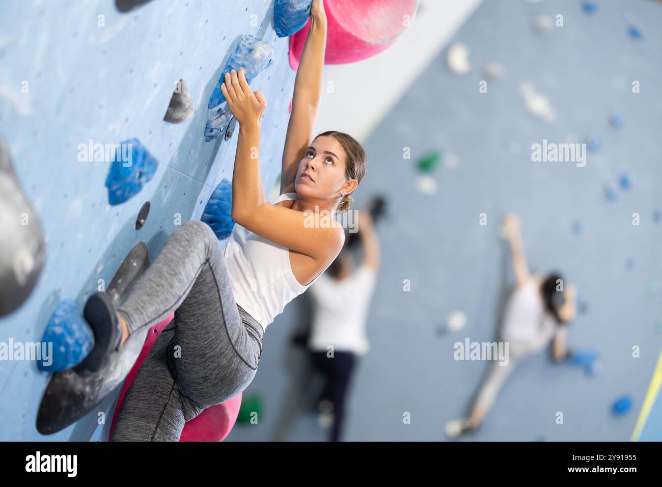 Donna sportiva che si arrampica su una parete di roccia artificiale nella palestra di arrampicata Foto Stock