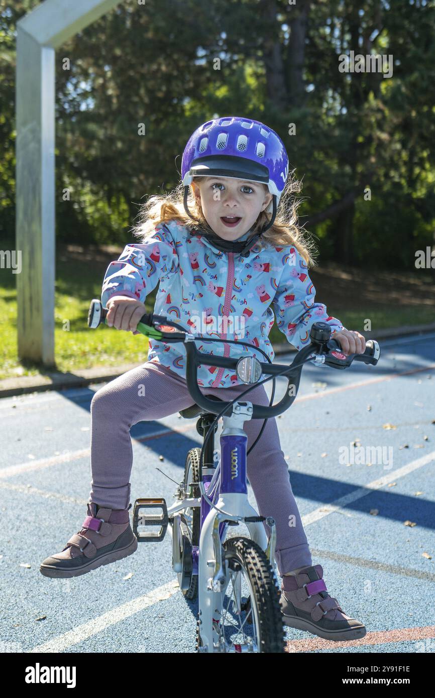 Ragazza con casco viola sorridente in sella a una bicicletta su un sentiero soleggiato del parco Foto Stock