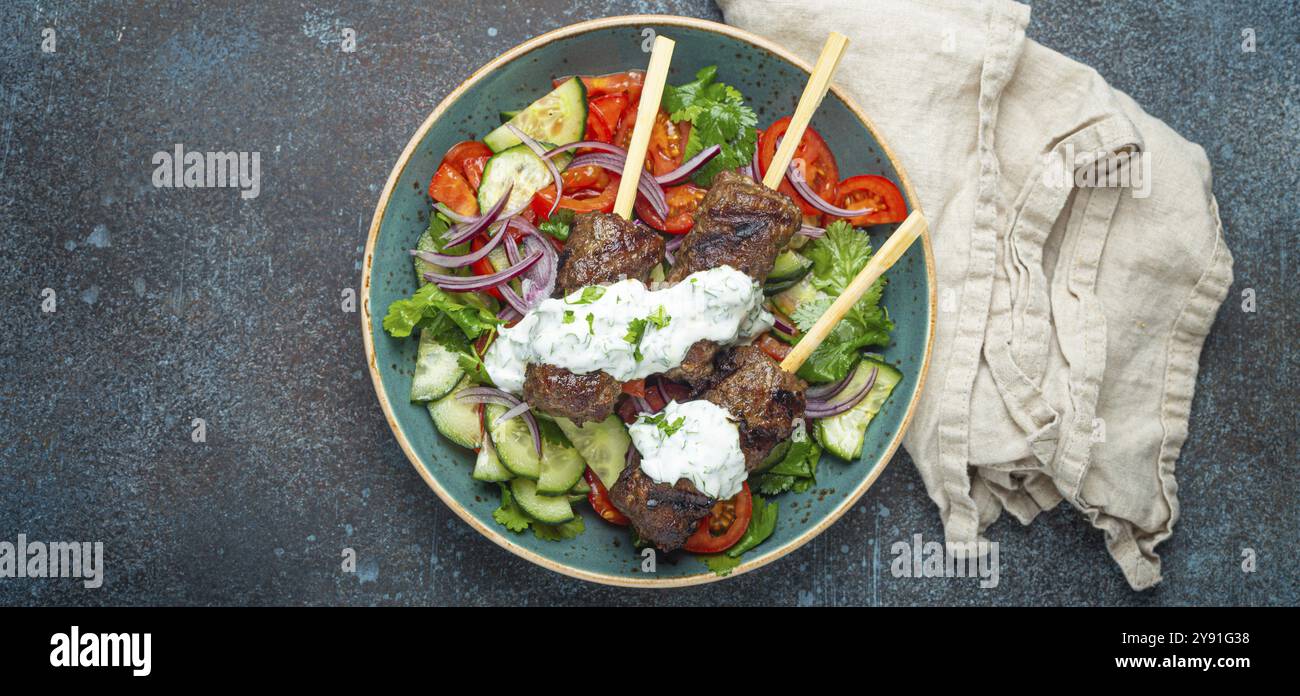 Spiedini grigliati di carne di manzo spiedini su bastoncini serviti con insalata di verdure fresche su piatto su sfondo rustico di cemento dall'alto. EAS centrale tradizionale Foto Stock