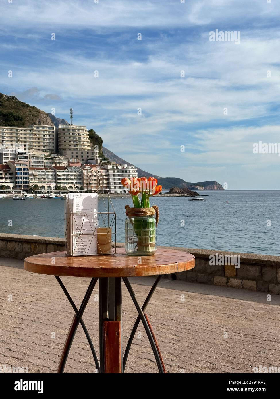 Un tavolo con un bouquet di tulipani e una pila di menu sull'argine di Rafailovici nella giornata di sole, Montenegro Foto Stock