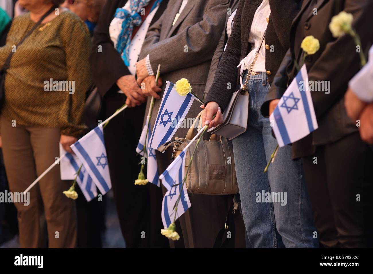 Dettagli con le mani di un uomo che regge la bandiera israeliana e un fiore durante una cerimonia commemorativa degli attacchi dell'ottobre 2023. Foto Stock