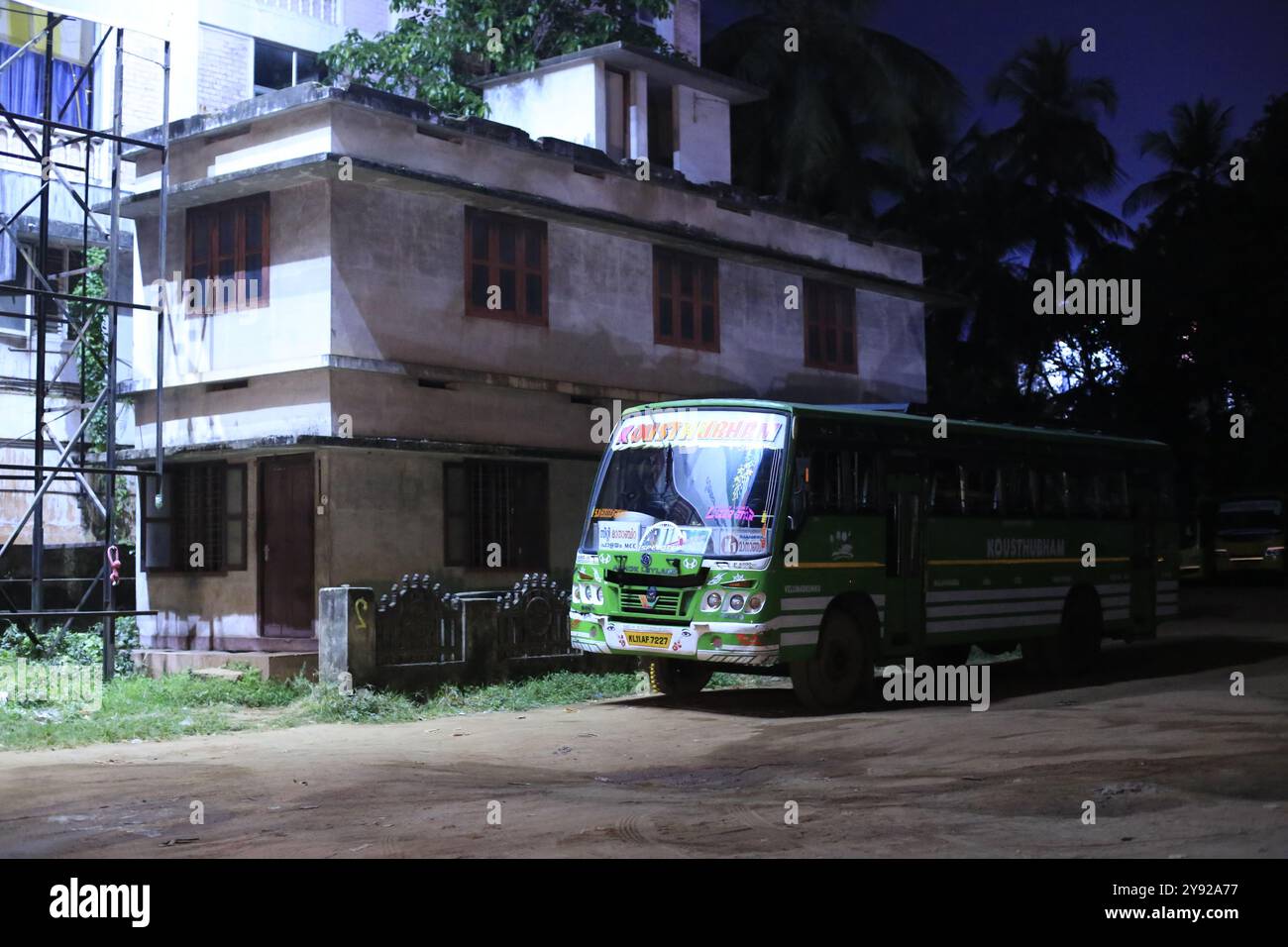 Una strada rurale di notte, con un autobus verde parcheggiato vicino ad un edificio tranquillo, illuminato da lampioni in una zona tranquilla. Foto Stock