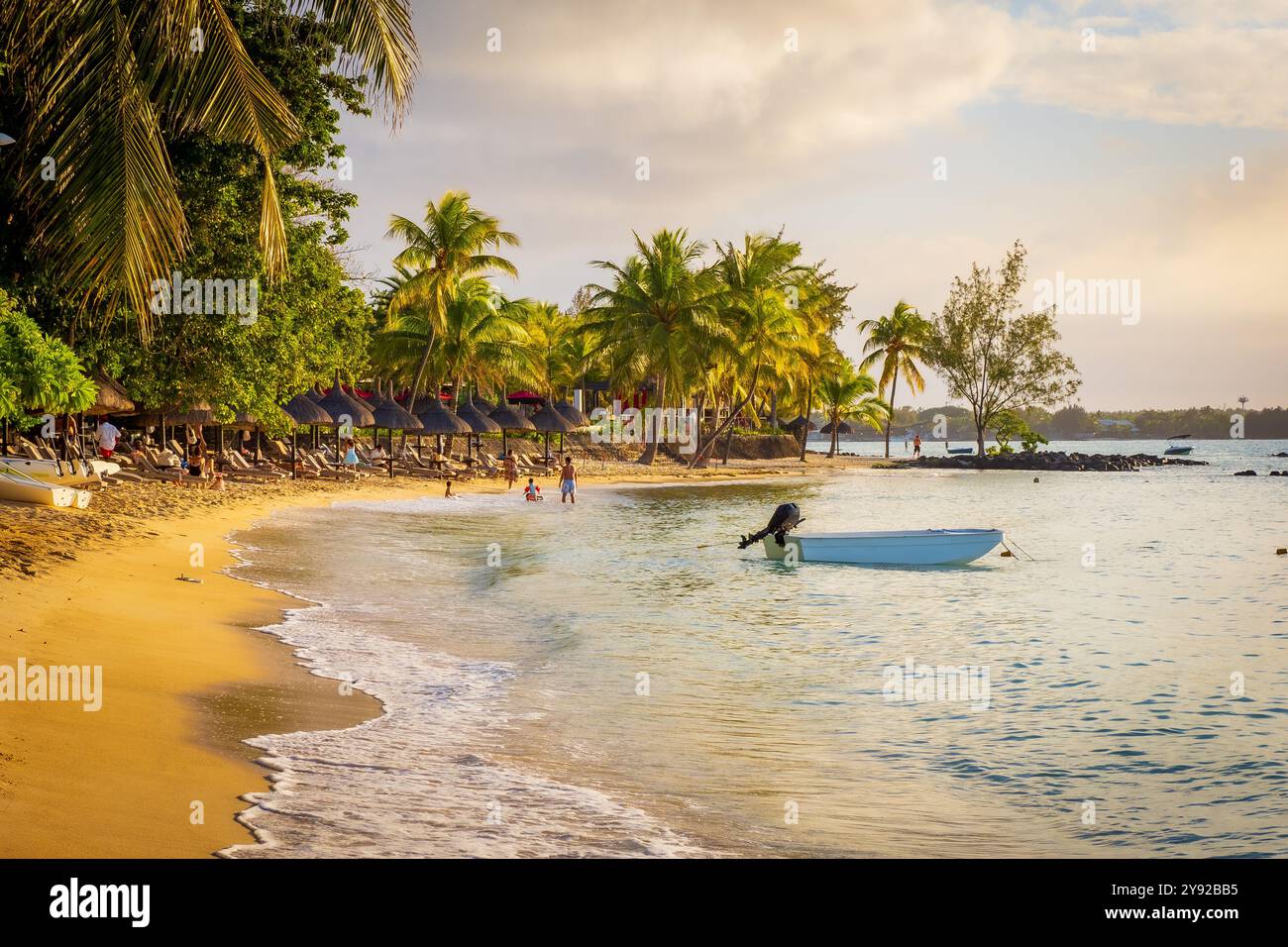 Splendida vista della splendida spiaggia tropicale di Grand Baie, Mauritius, con sabbia fine e fiancheggiata da alberi di cocco al tramonto durante l'ora d'oro Foto Stock