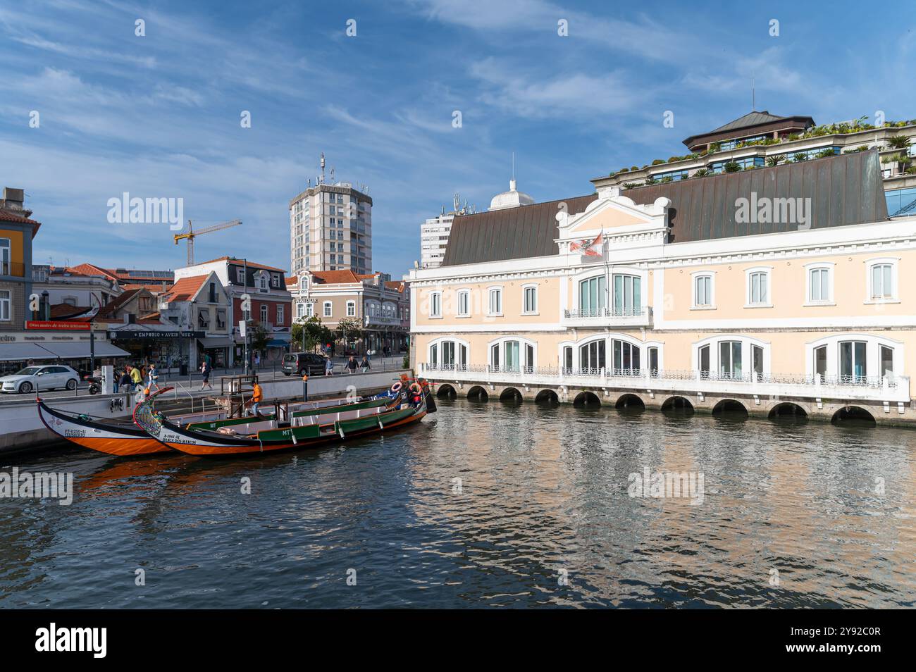 Aveiro, Portogallo - 11 settembre 2024 : barche colorate sono ormeggiate vicino ad un affascinante edificio sul fiume sotto un cielo limpido. Foto Stock