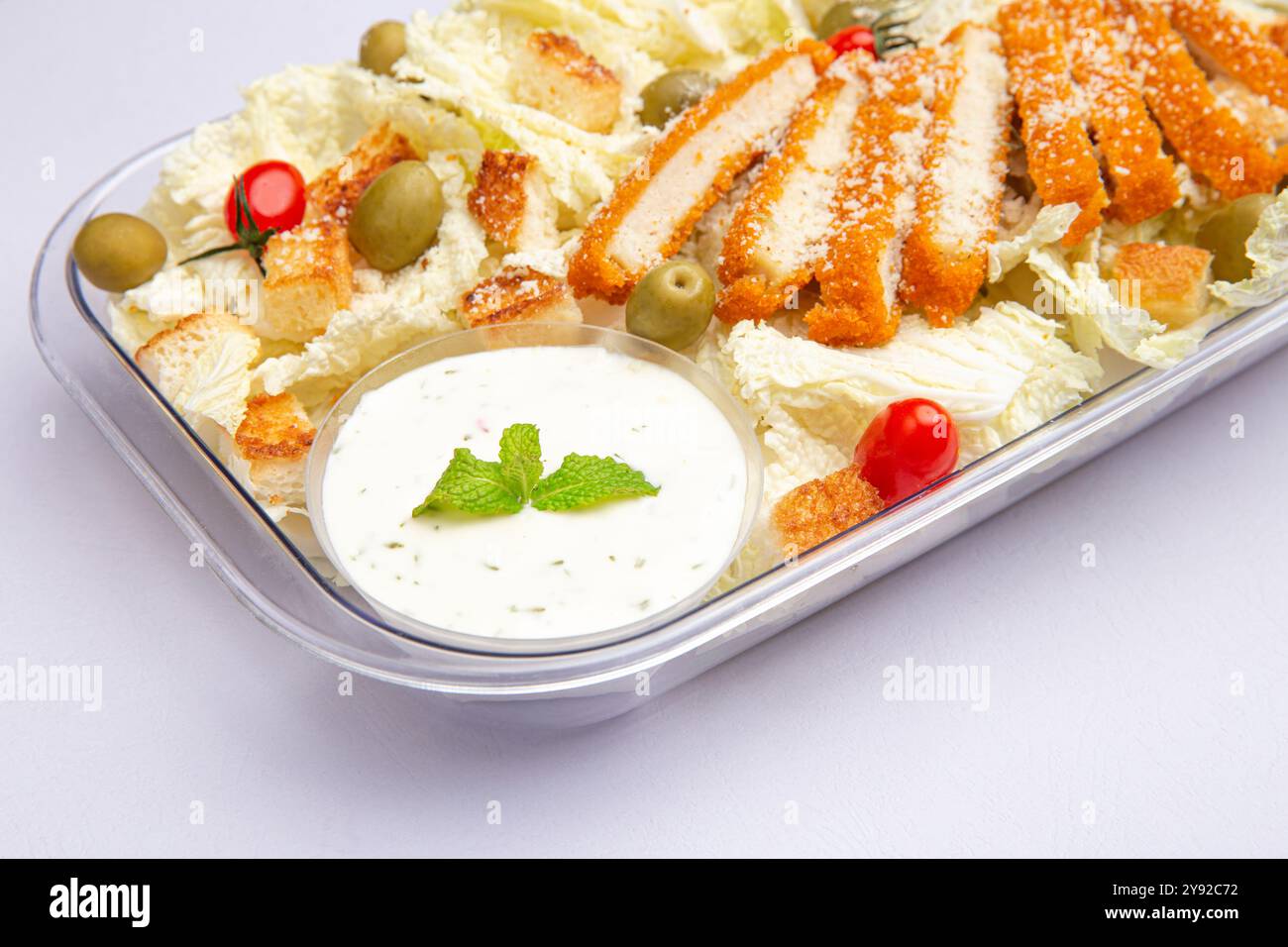 Insalata croccante di pollo con olive, pomodori ciliegini, crostini e condimento cremoso in un recipiente trasparente. Foto Stock