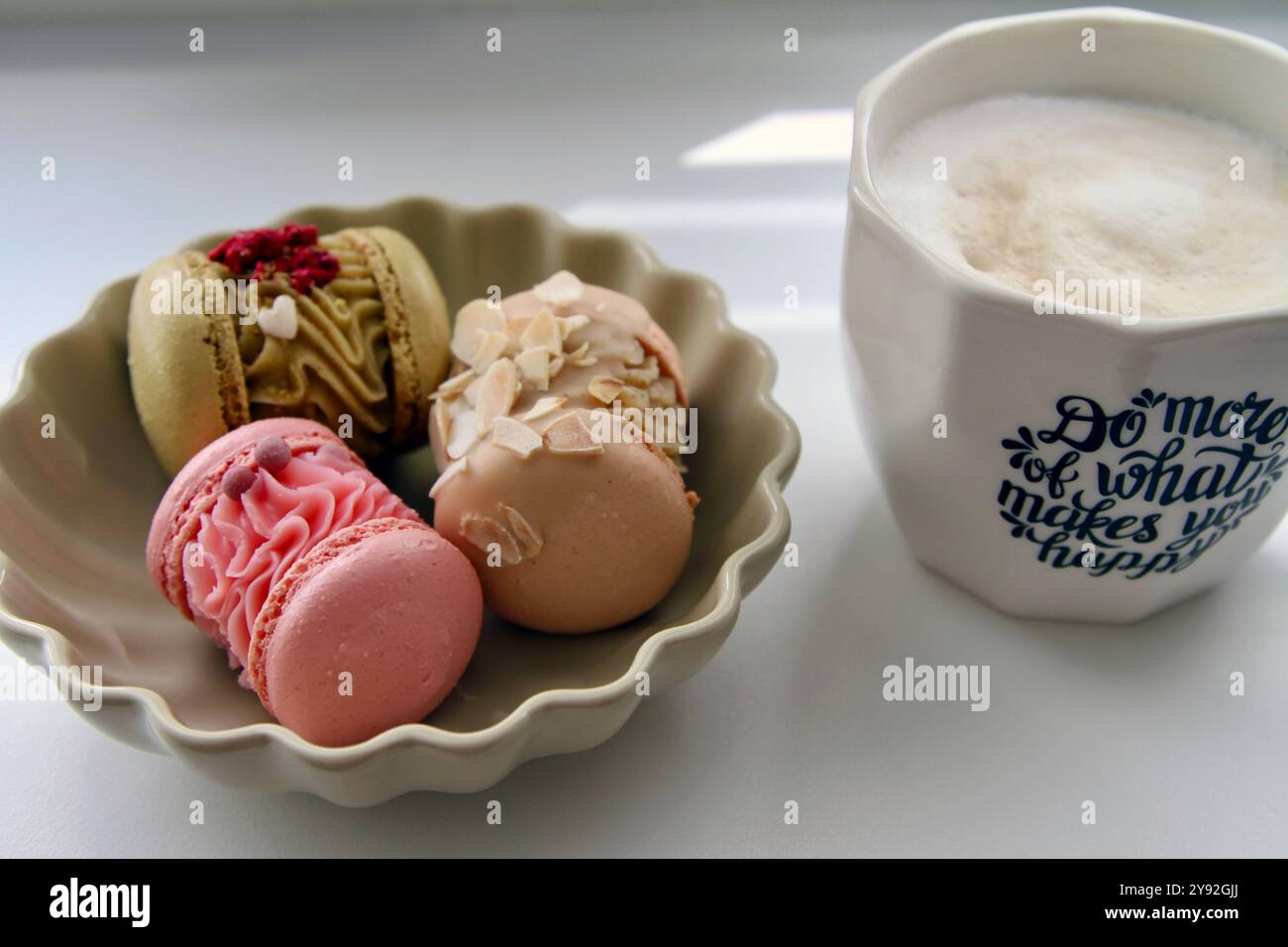 Tazza di caffè bianco e macaron in diversi colori e gusti nel piatto beige Foto Stock