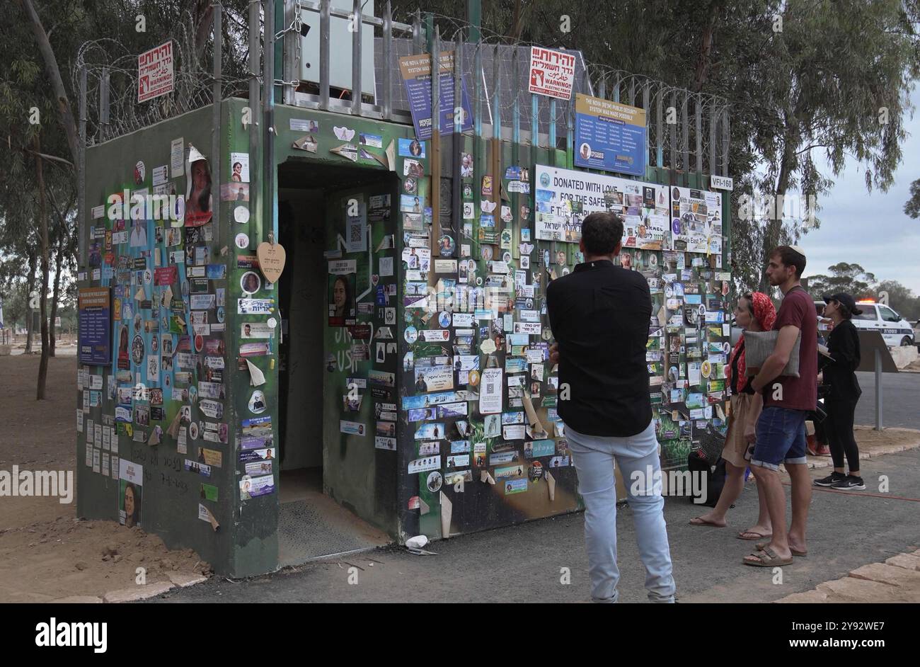 RE'IM, ISRAELE - 7 OTTOBRE: Gli israeliani guardano a un rifugio antiatomico pubblico indipendente chiamato Migunit (in ebraico) con adesivi commemorativi che commemorano i soldati IDF uccisi nella guerra israeliana a Gaza e ter­ror vic­tims dopo Octo­ber 7, mentre i familiari e gli amici dei perduti e rapiti si riuniscono nel sito del Nova Festival per celebrare l'anniversario degli attacchi di Hamas il 7 ottobre 2024 a Re'im, Israele. Foto Stock