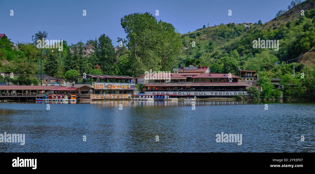 Lago di sera Gölü (lago Trabzon) a Trabzon, Turchia, vista della luce del giorno con persone in barca e ristoranti sullo sfondo. Foto Stock