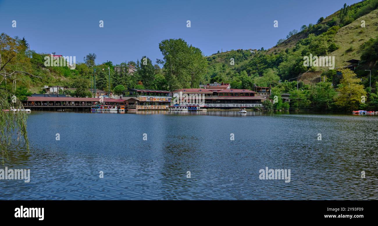 Lago di sera Gölü (lago Trabzon) a Trabzon, Turchia, vista della luce del giorno con persone in barca e ristoranti sullo sfondo. Foto Stock