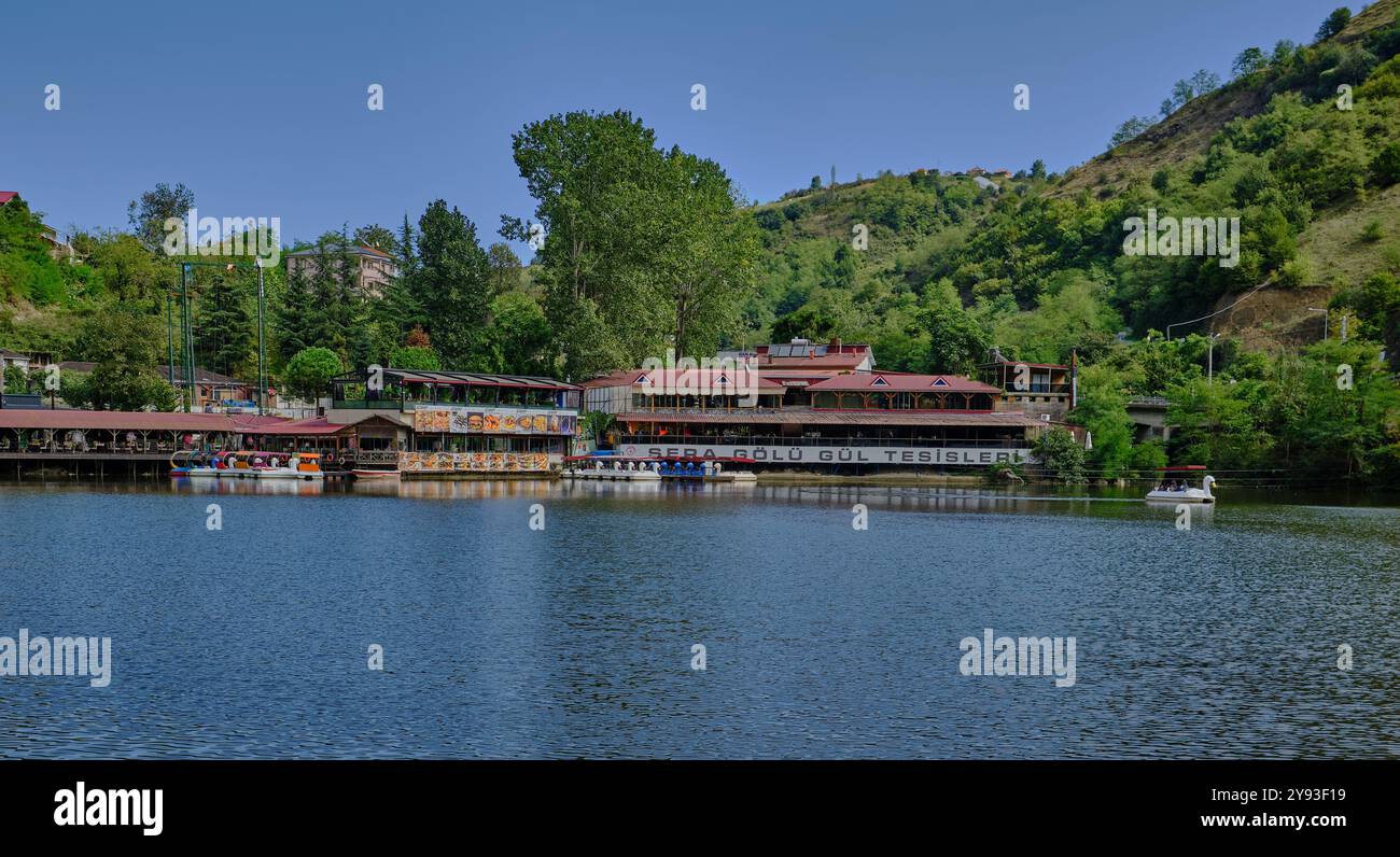 Lago di sera Gölü (lago Trabzon) a Trabzon, Turchia, vista della luce del giorno con persone in barca e ristoranti sullo sfondo. Foto Stock