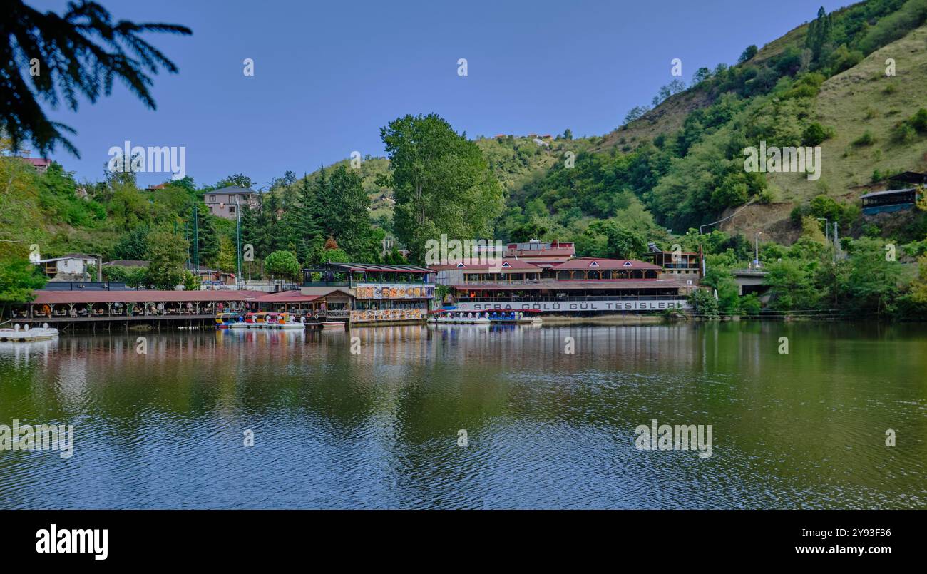 Lago di sera Gölü (lago Trabzon) a Trabzon, Turchia, vista della luce del giorno con persone in barca e ristoranti sullo sfondo. Foto Stock
