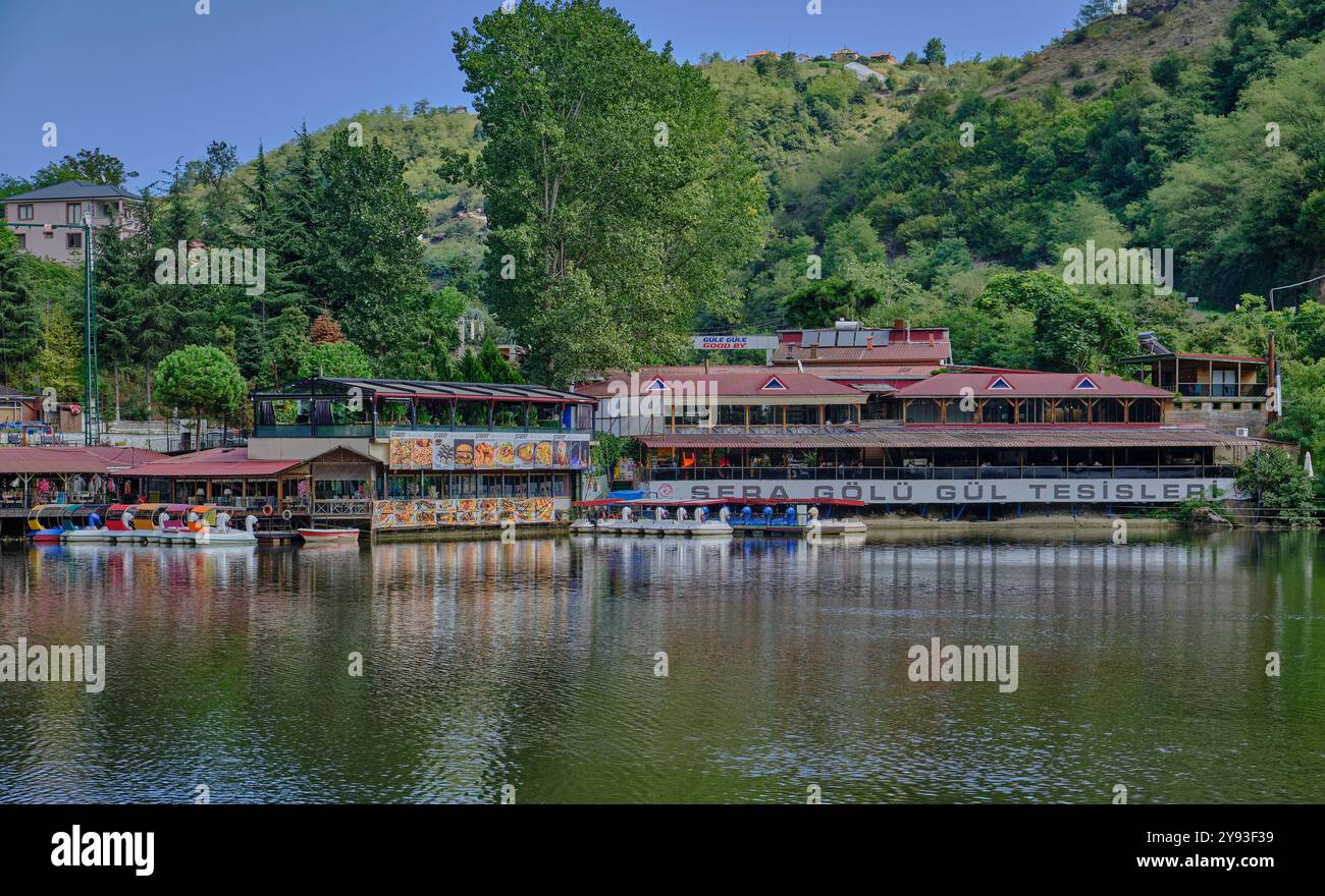 Lago di sera Gölü (lago Trabzon) a Trabzon, Turchia, vista della luce del giorno con persone in barca e ristoranti sullo sfondo. Foto Stock