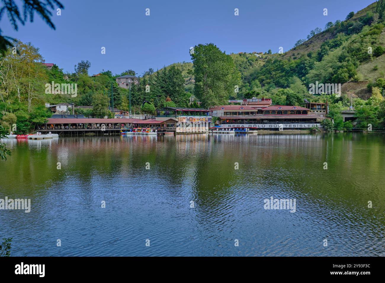 Lago di sera Gölü (lago Trabzon) a Trabzon, Turchia, vista della luce del giorno con persone in barca e ristoranti sullo sfondo. Foto Stock