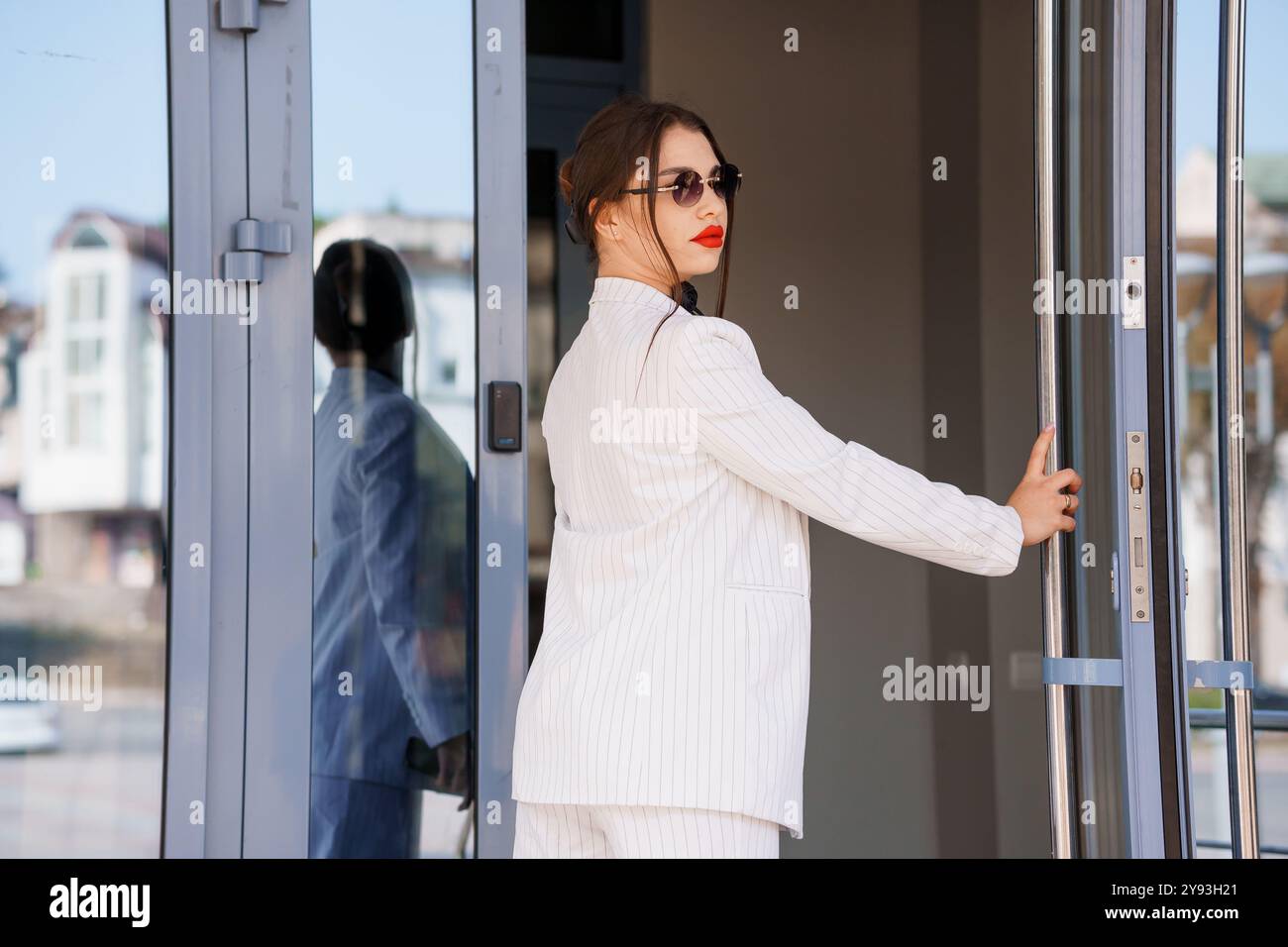 Elegante donna d'affari che esce dal moderno edificio per uffici con sicurezza e stile. Foto Stock