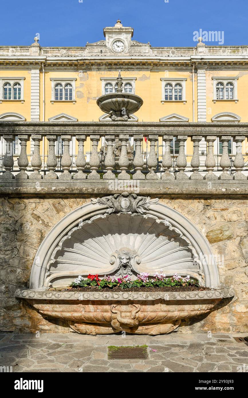 Fontana in pietra piena di piante fiorite con il municipio della località turistica sulla Riviera Ligure sullo sfondo, Alassio, Liguria, Italia Foto Stock
