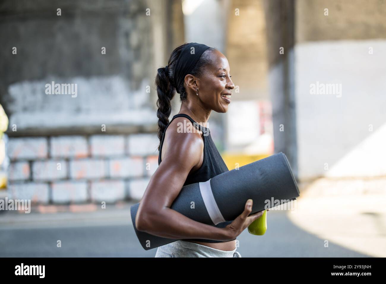 Donna sorridente che tiene un tappetino per esercizi in città Foto Stock