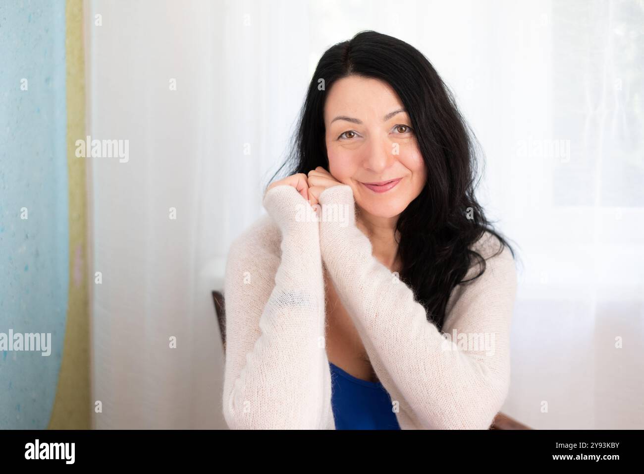 Donna elegante che sorride in un ambiente accogliente, outfit casual, luce naturale, atmosfera gioiosa, atmosfera mattutina, ritratto interno, rilassato, momento di stile di vita, se Foto Stock