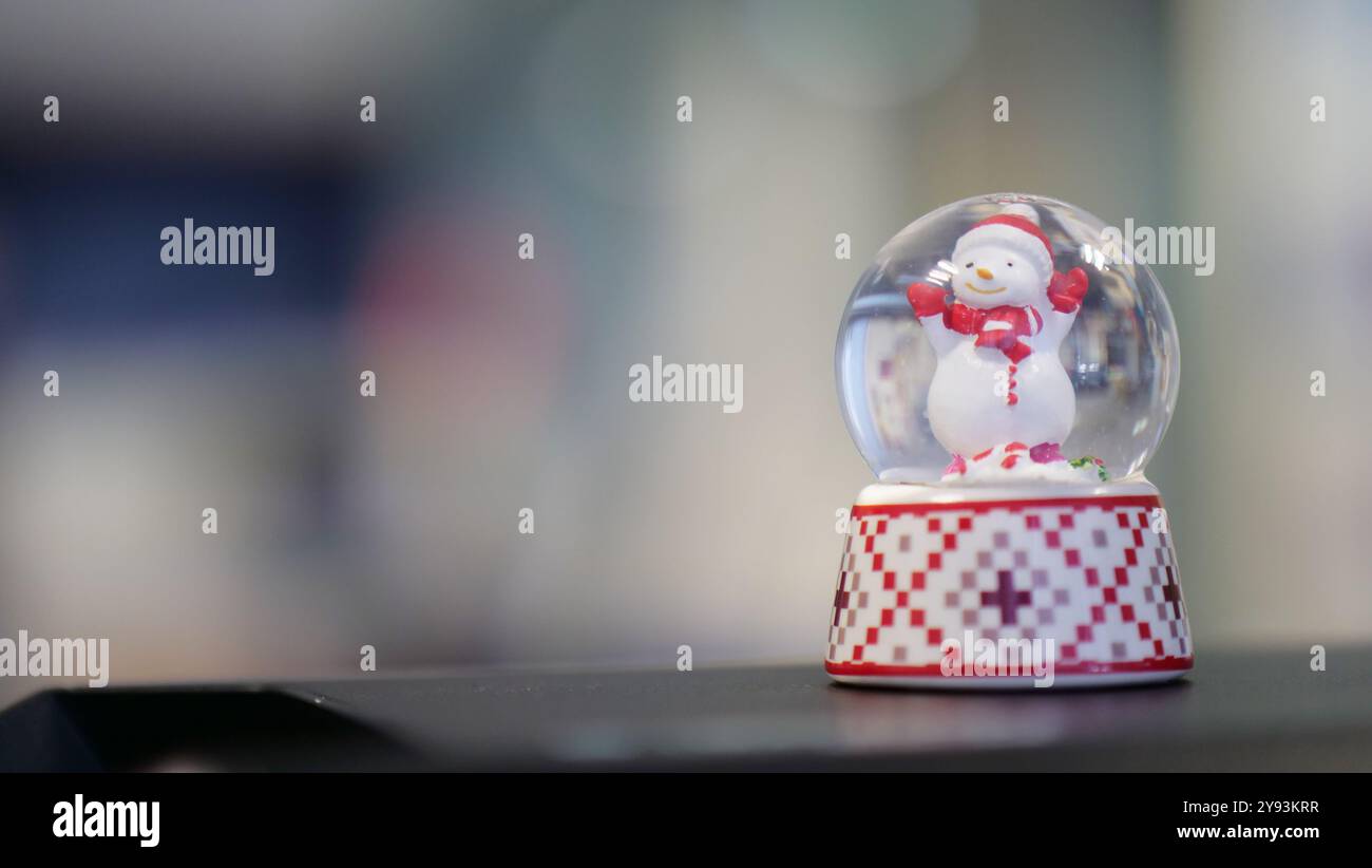 Un globo di neve con un allegro pupazzo di neve, ambientato su uno sfondo sfocato. La base ha un motivo a scacchi rosso e bianco con accenti verdi Foto Stock