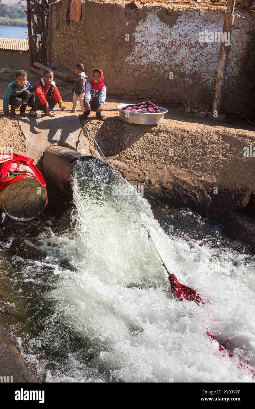 I bambini lavano i vestiti in uno scarico che pompano acqua dal Nilo per fornire un canale di irrigazione delle colture intorno al villaggio di Ramadi, in Egitto Foto Stock