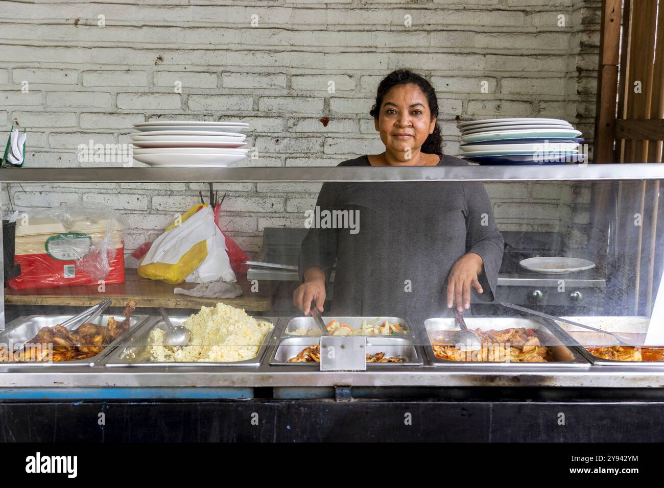 Una donna in El Salvador si trova dietro una bancarella di cibo, che serve cibo di strada tradizionale salvadoregno. L'esposizione include diversi piatti con uno sfondo di Foto Stock