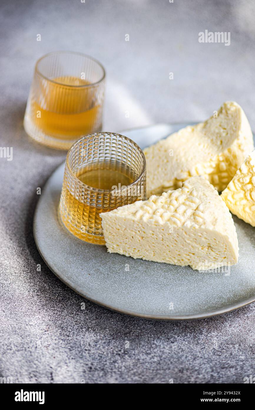 Formaggio Sulguni georgiano abbinato al vino ambrato, una variante di vino bianco georgiano secco, presentato elegantemente su un piatto grigio Foto Stock