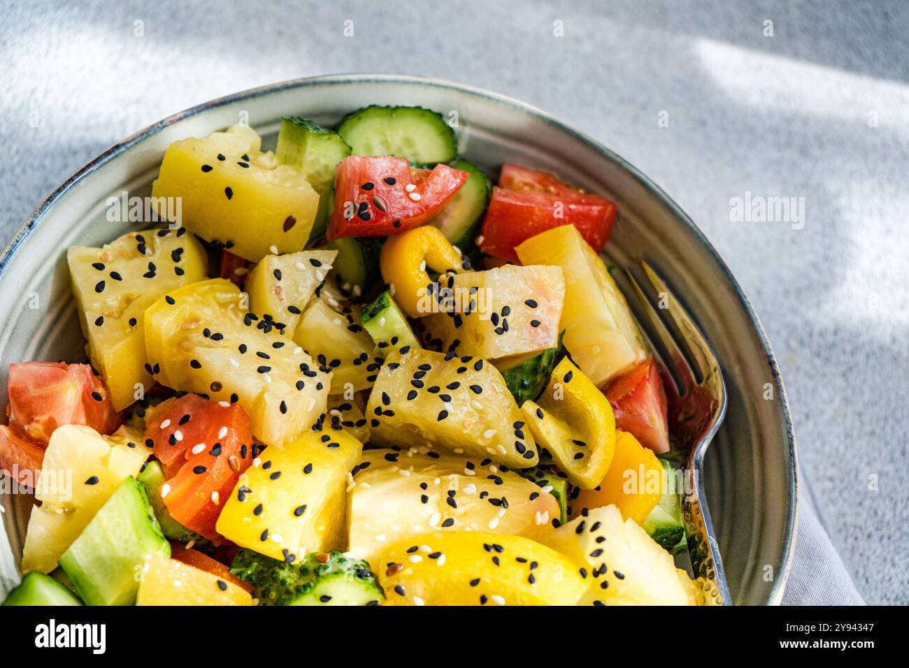 Vista dall'alto di un'insalata di verdure colorata con pomodori rossi e gialli, cetrioli, peperoni e cosparsi di semi di sesamo, serviti in una ciotola. Foto Stock