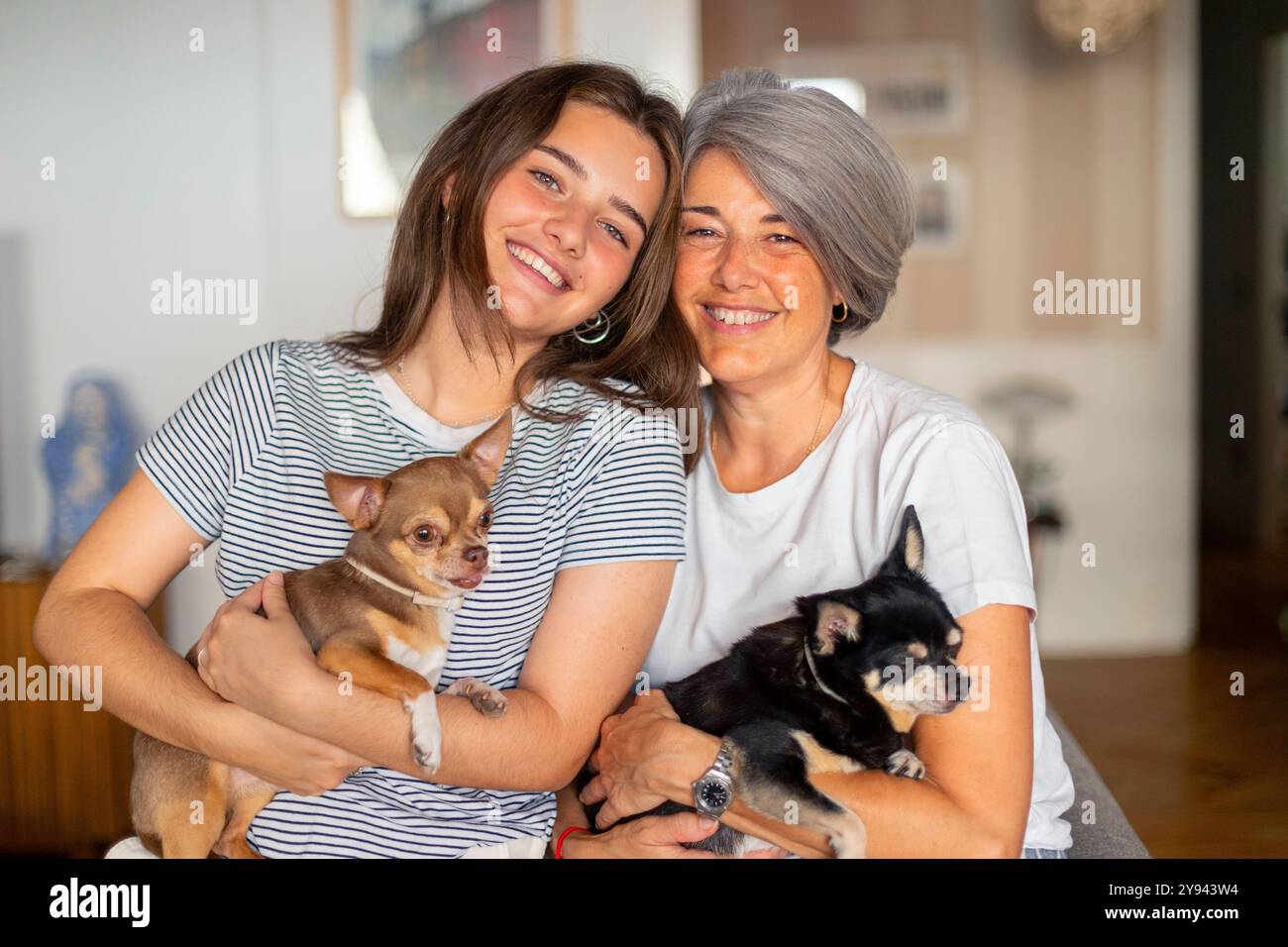 Una scena commovente di una madre e sua figlia, sorridenti e con due cani piccoli, che mostrano un'atmosfera familiare e accogliente i setti interni Foto Stock