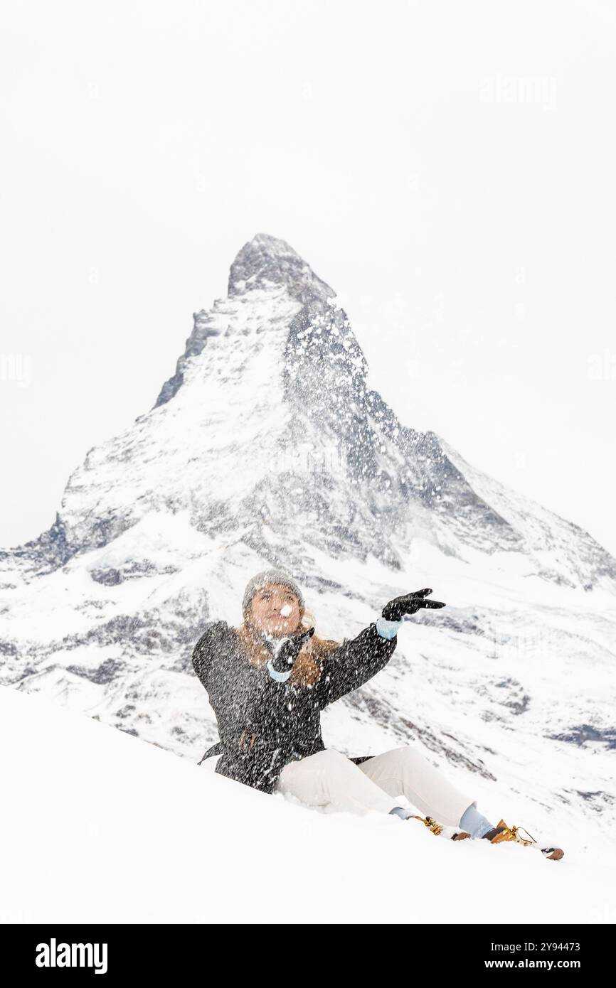 Una gioiosa donna asiatica gioca sulla neve, estendendo con grazia il braccio, godendosi una giornata invernale con la montagna del Cervino alle sue spalle nelle alpi svizzere. Foto Stock