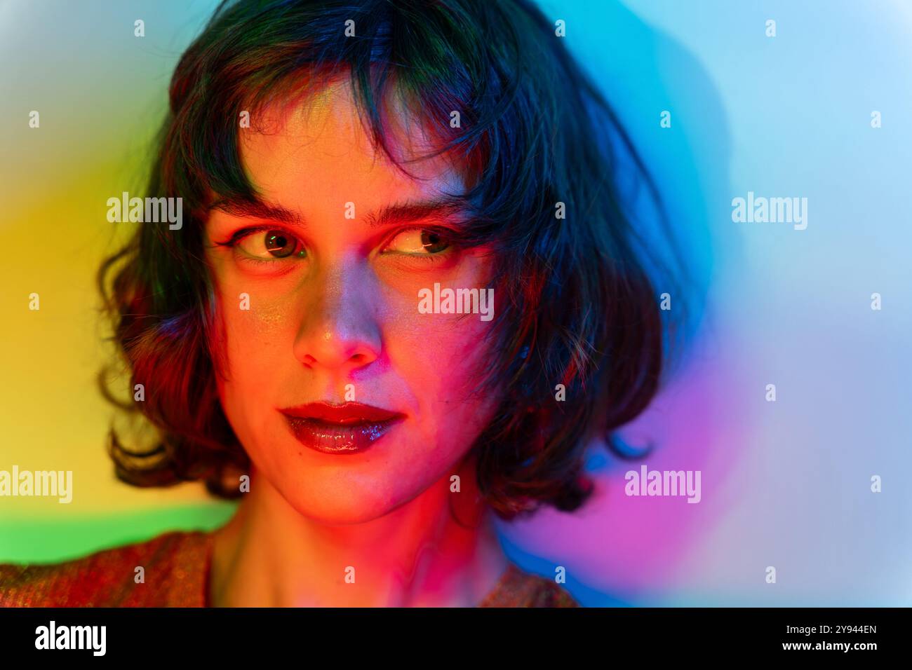 Foto ravvicinata di una giovane donna immersa in una luce multicolore, che crea un effetto visivo vibrante e drammatico. Il suo sguardo misterioso si aggiunge agli intens Foto Stock