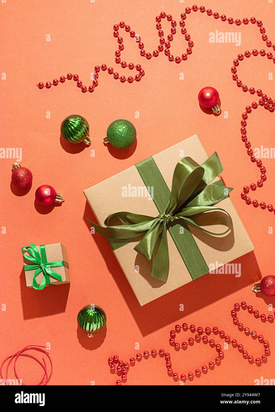 Una vista aerea dei regali di Natale avvolti in carta ecologica adornata con nastri verdi di raso, circondata da baubles rosse e verdi e scintillanti Foto Stock