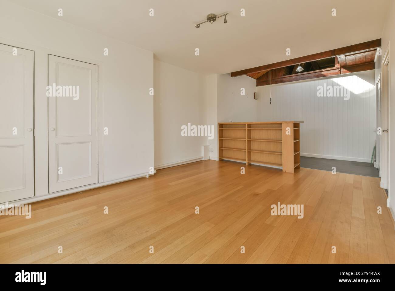 Una camera vuota con pavimento in legno, pareti bianche e una piccola libreria in legno sotto un'area con loft. Foto Stock