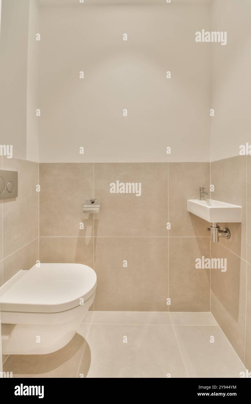 Un bagno contemporaneo con WC a parete e lavandino angolare con pareti piastrellate e pavimento in tonalità neutre. Foto Stock