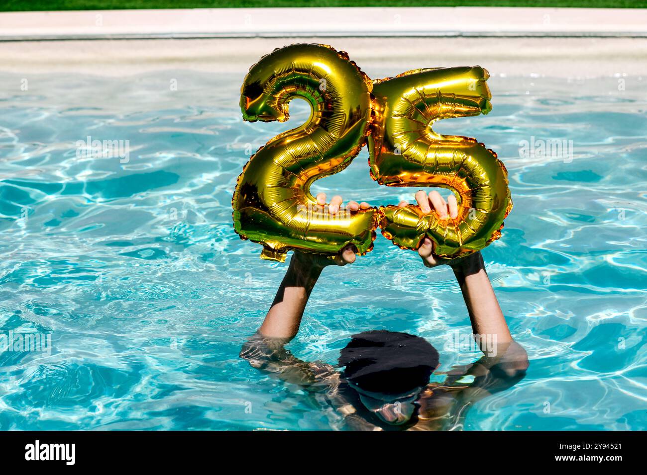 Persona irriconoscibile che tiene in mano palloncini dorati numero 25 in una piscina, per celebrare un'occasione speciale. Foto Stock