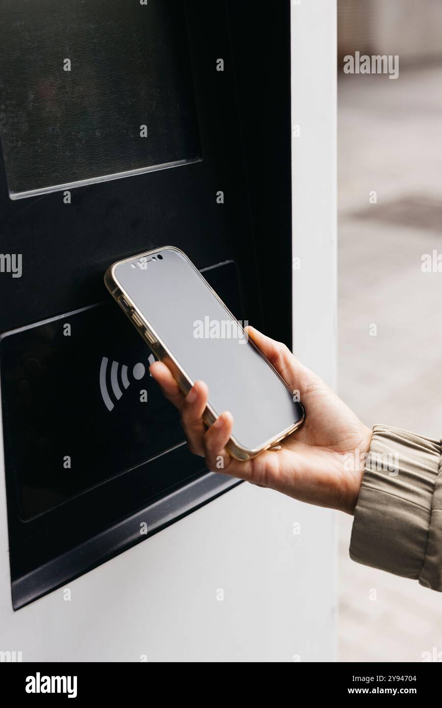 Primo piano di una mano che tiene uno smartphone in una stazione di ricarica per auto, donna che effettua un pagamento contactless per caricare la sua auto per veicoli elettrici. Foto Stock