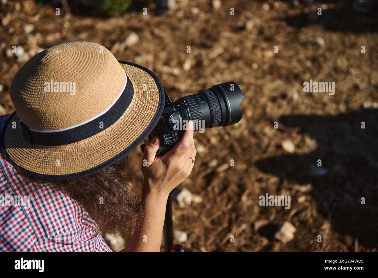 Un fotografo che indossa un cappello di paglia si concentra sull'acquisizione di paesaggi all'aperto con una fotocamera, creando una composizione artistica alla luce del sole naturale. Foto Stock