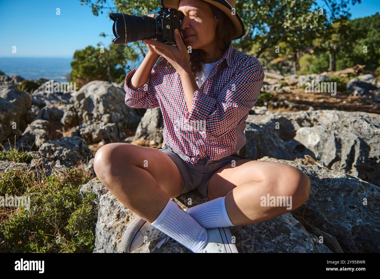 Avventura all'aperto con donna che cattura la bellezza della natura in una natura rocciosa selvaggia. Vestita in modo informale, indossa un cappello, una camicia e pantaloncini corti, che incarnano tra Foto Stock