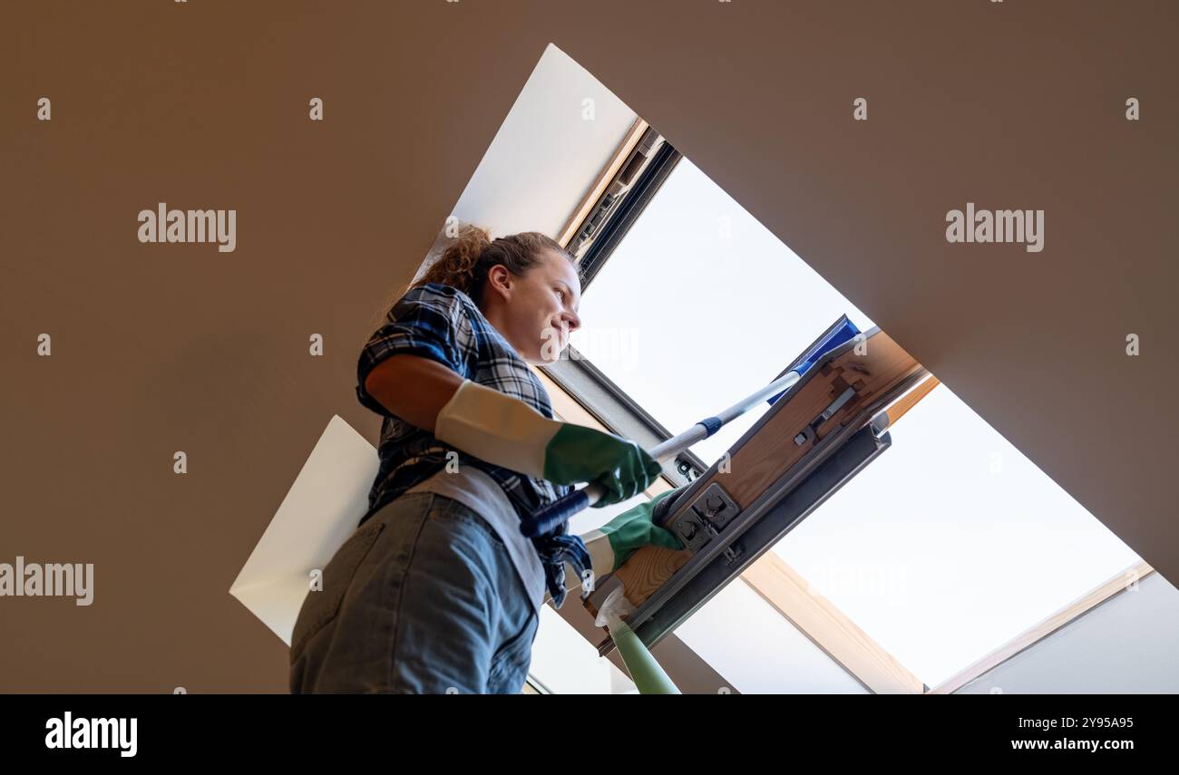 Una donna che lava e pulisce una finestra lucernario a casa. Foto Stock