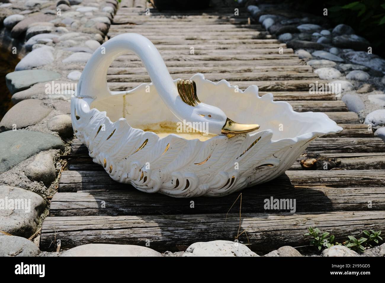 Su un pittoresco ponte di legno, si trova un cesto splendidamente realizzato a forma di un grazioso cigno bianco, che crea una scena elegante Foto Stock