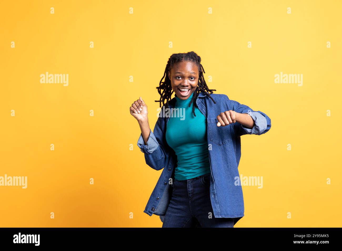 Allegra adolescente afroamericana che fa danza felice, si sente gioiosa, isolata sullo sfondo dello studio. Ritratto di una persona felice che celebra il raggiungimento, mostrando un comportamento positivo Foto Stock