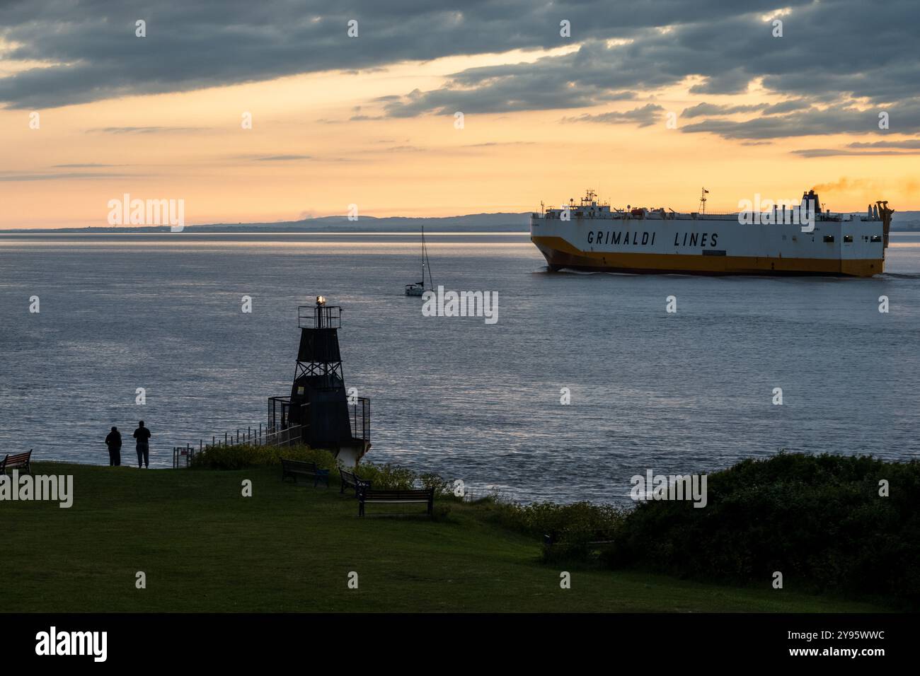Una grande nave da carico e un piccolo yacht a vela passano nel Canale di Bristol al largo della costa di Portishead nel Somerset. Foto Stock