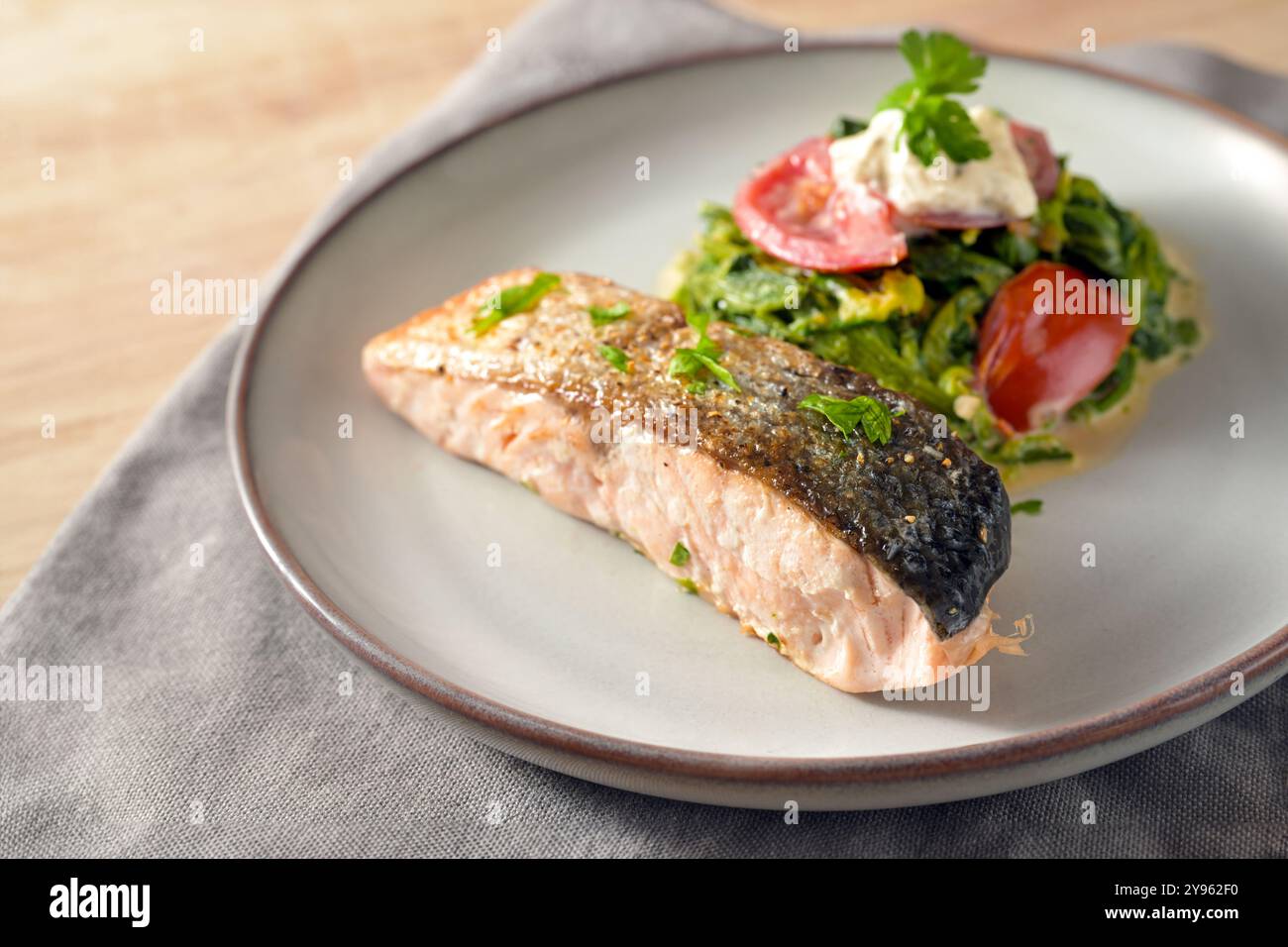 Filetto di salmone arrostito con una pelle croccante, verdure di panna di spinaci, cipolle, pomodori e guarnigioni di prezzemolo, sana farina di pesce su un piatto grigio, basso Foto Stock