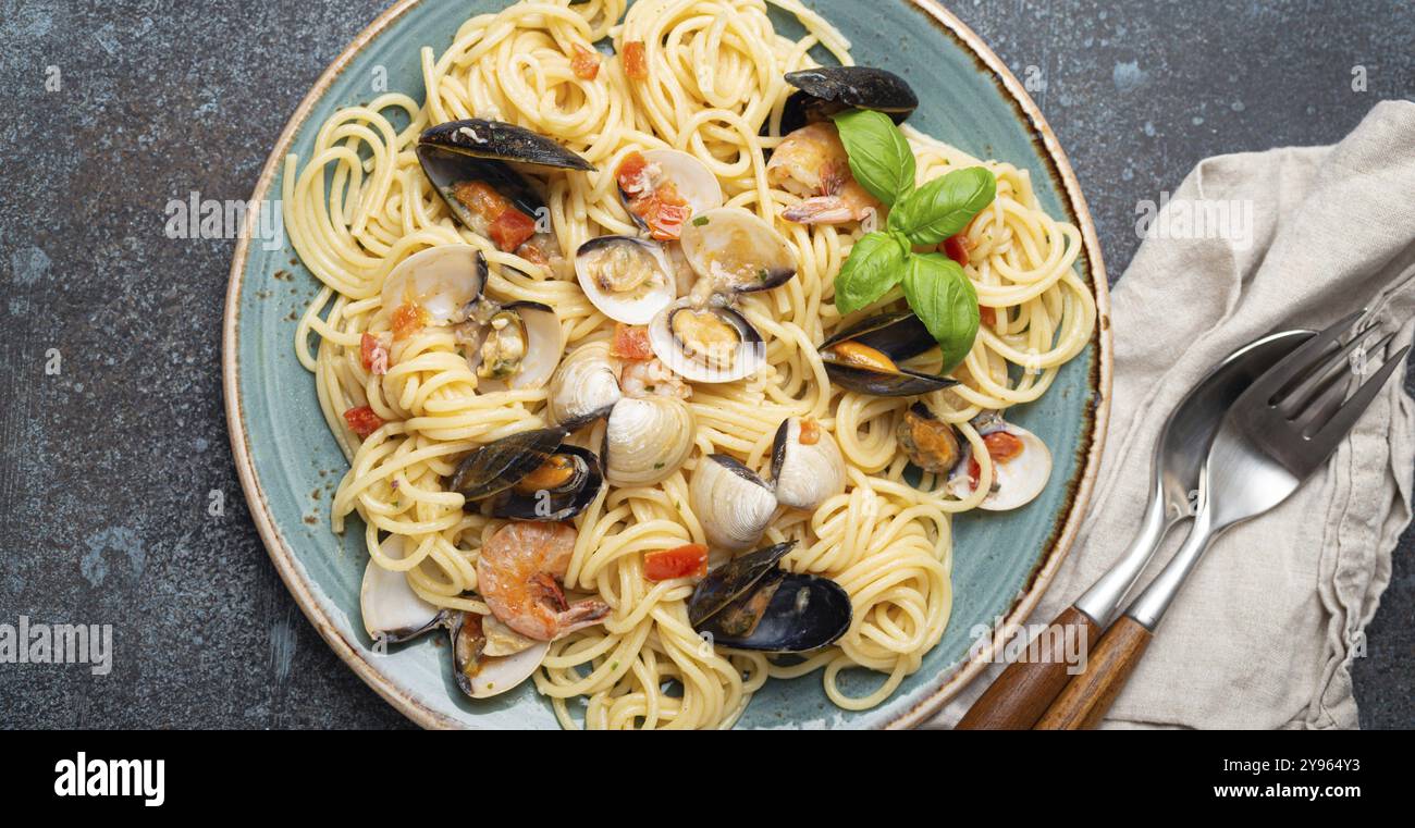 Spaghetti di pasta italiana di pesce con cozze, gamberetti, vongole in salsa di pomodoro con basilico verde sul piatto su fondo rustico in cemento blu sopra la testa. Io Foto Stock