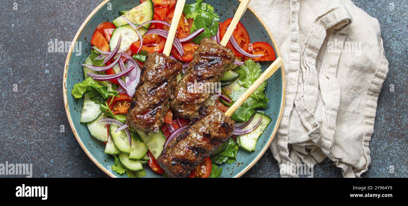 Spiedini grigliati di carne di manzo spiedini su bastoncini serviti con insalata di verdure fresche su piatto su sfondo rustico di cemento dall'alto. EAS centrale tradizionale Foto Stock