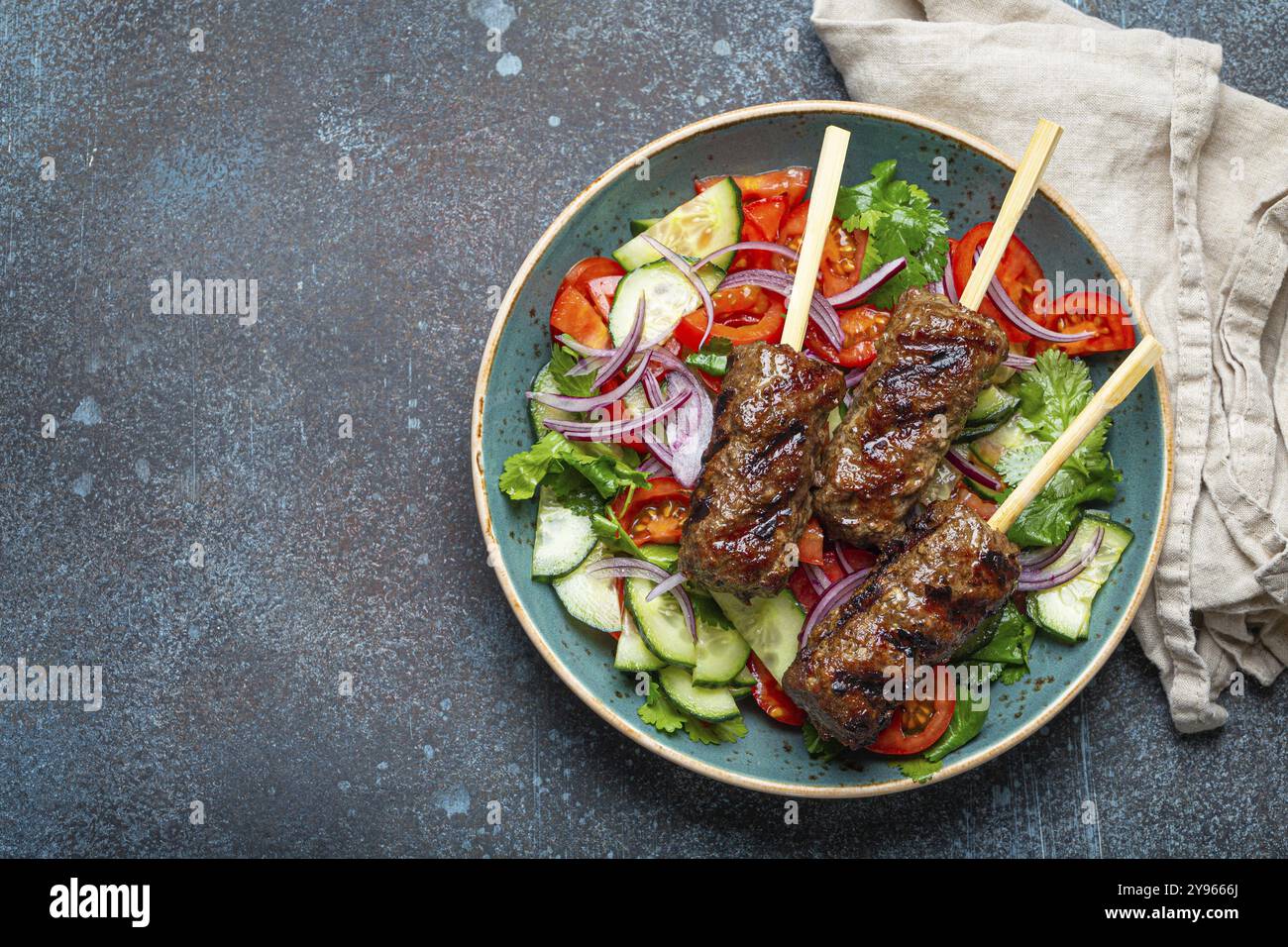 Spiedini grigliati di carne di manzo spiedini su bastoncini serviti con insalata di verdure fresche su piatto su sfondo rustico di cemento dall'alto. EAS centrale tradizionale Foto Stock